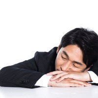 昼休みに机にうつぶせ寝する疲れた会社員の休憩風景の写真