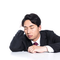 勤務中にテーブルで居眠りするサラリーマンの写真
