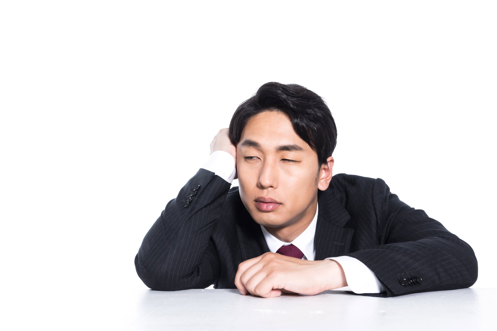 机に突っ伏して居眠りをする黒いスーツ姿のサラリーマン［モデル：大川竜弥］