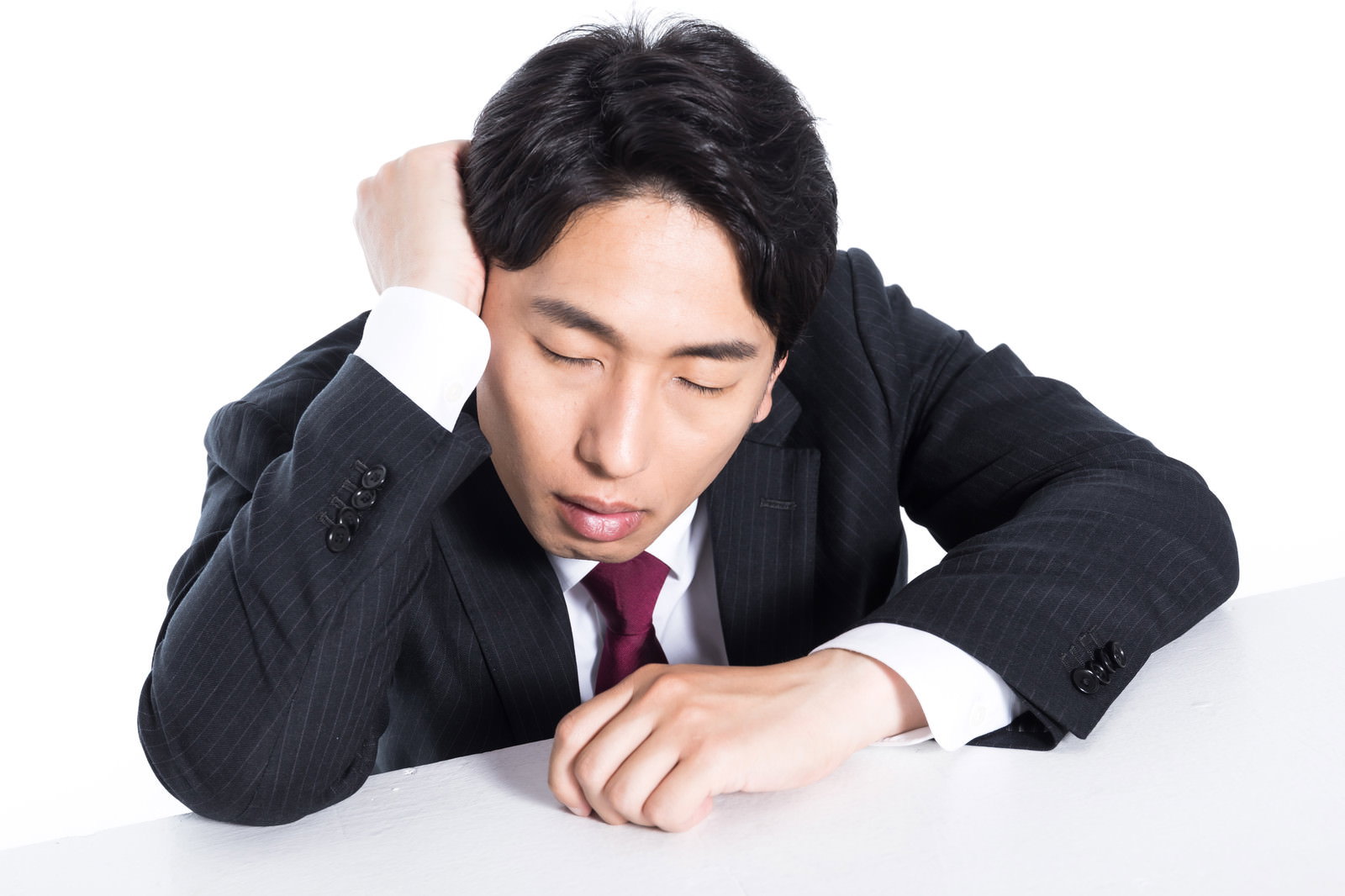 机に突っ伏して眠る疲れたスーツ姿の男性ビジネスマン［モデル：大川竜弥］