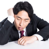 机に突っ伏して眠るビジネスマン｜残業と過労の写真