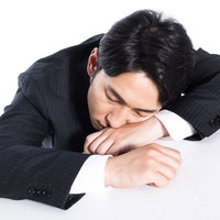 連日の残業で机にうつ伏せで寝落ちする会社員男性の写真