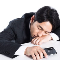 スマートフォンを握ったまま寝落ちする会社員男性の写真