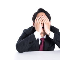 不正がバレて頭を抱える男性会社員のビジネストラブルの写真