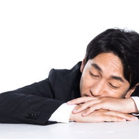机に突っ伏して昼寝する会社員の疲労と休憩の写真