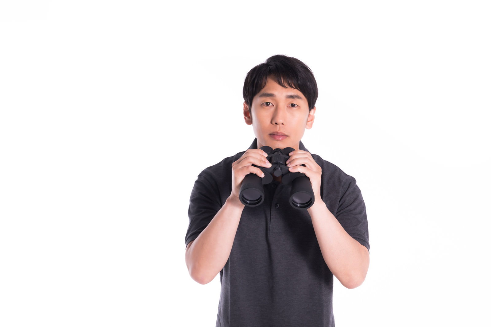 双眼鏡を両手で持ち、無表情で監視している黒いTシャツの男性［モデル：大川竜弥］