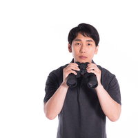 双眼鏡を構えて無表情で監視対象をウォッチする男性の写真