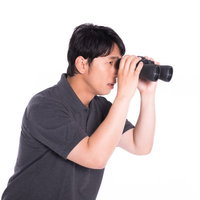 見えないものを見ようとして双眼鏡をのぞき込んだ男性の写真
