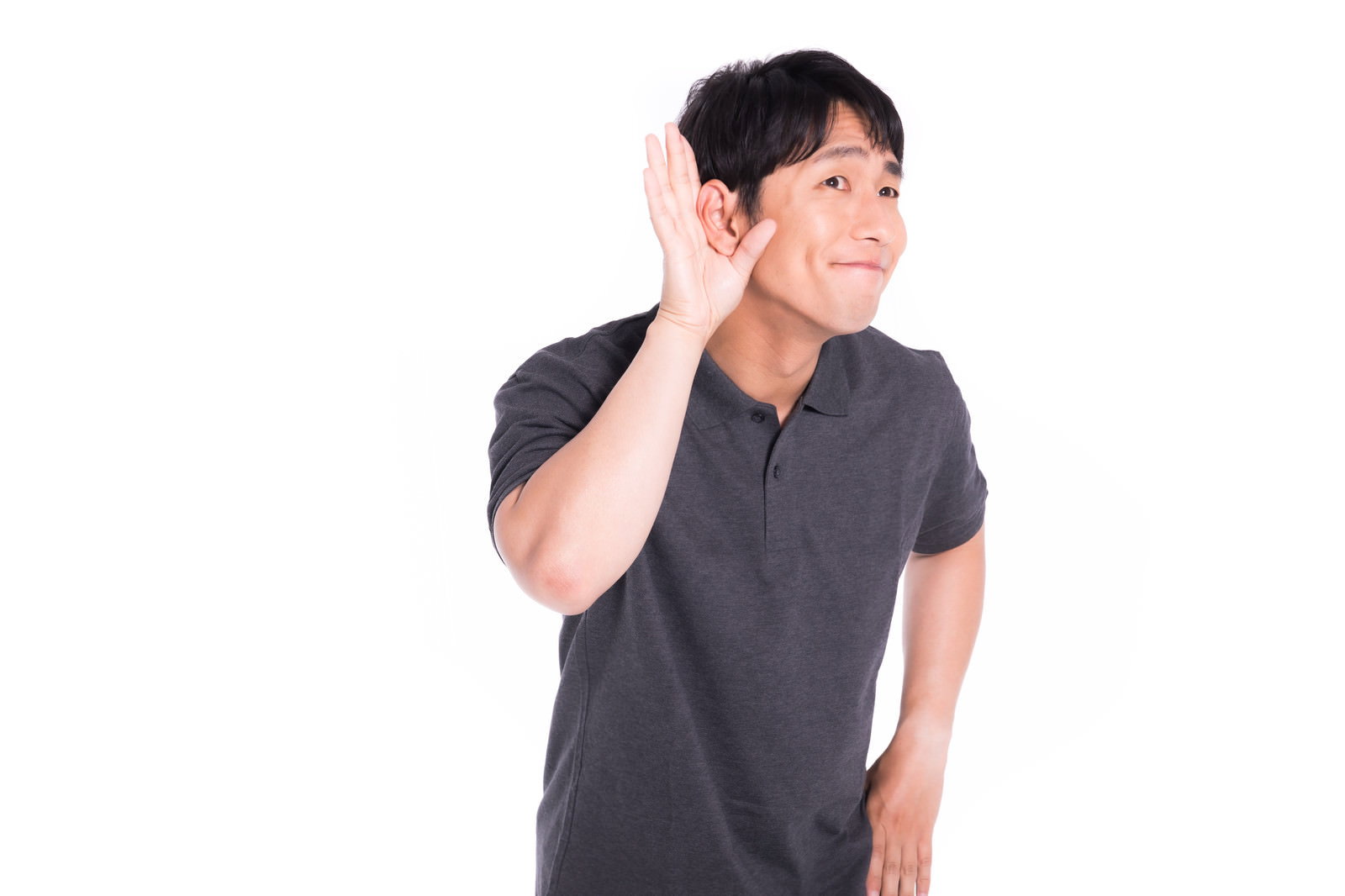 右手を耳に当てて聞き耳を立てるグレーのTシャツの男性［モデル：大川竜弥］