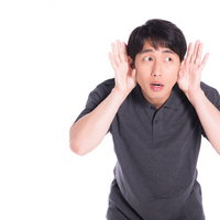 両手を耳に当てて音を聞き取ろうとする男性の写真