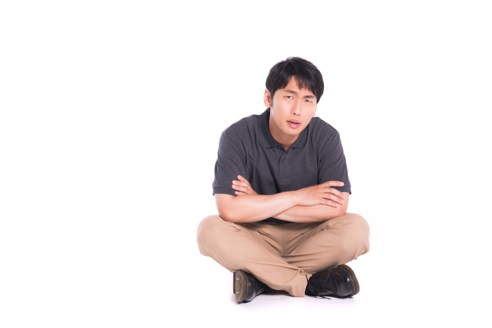 床に座り込んで腕を組み、不満そうな表情を見せる黒いTシャツの男性［モデル：大川竜弥］