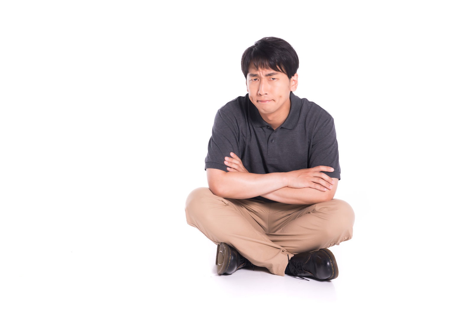 不満そうに腕を組んであぐらをかいて座る男性［モデル：大川竜弥］