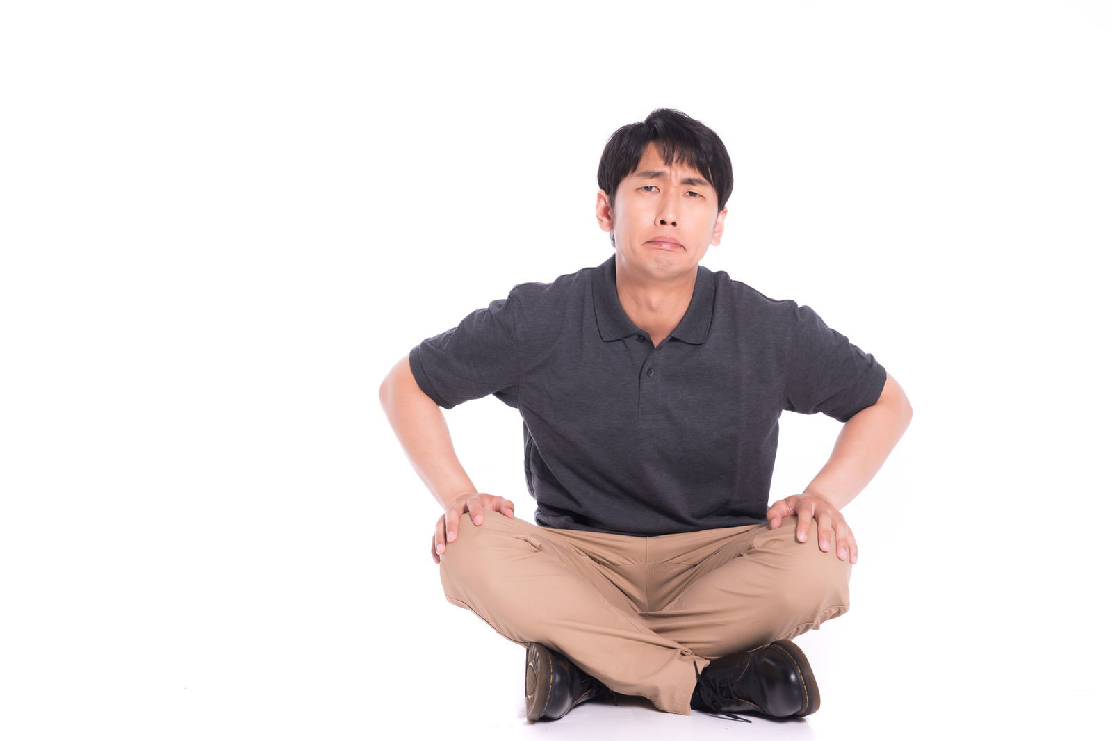 あぐらをかいて床に座り、腕を組んで正面を見つめる黒いシャツの男性［モデル：大川竜弥］