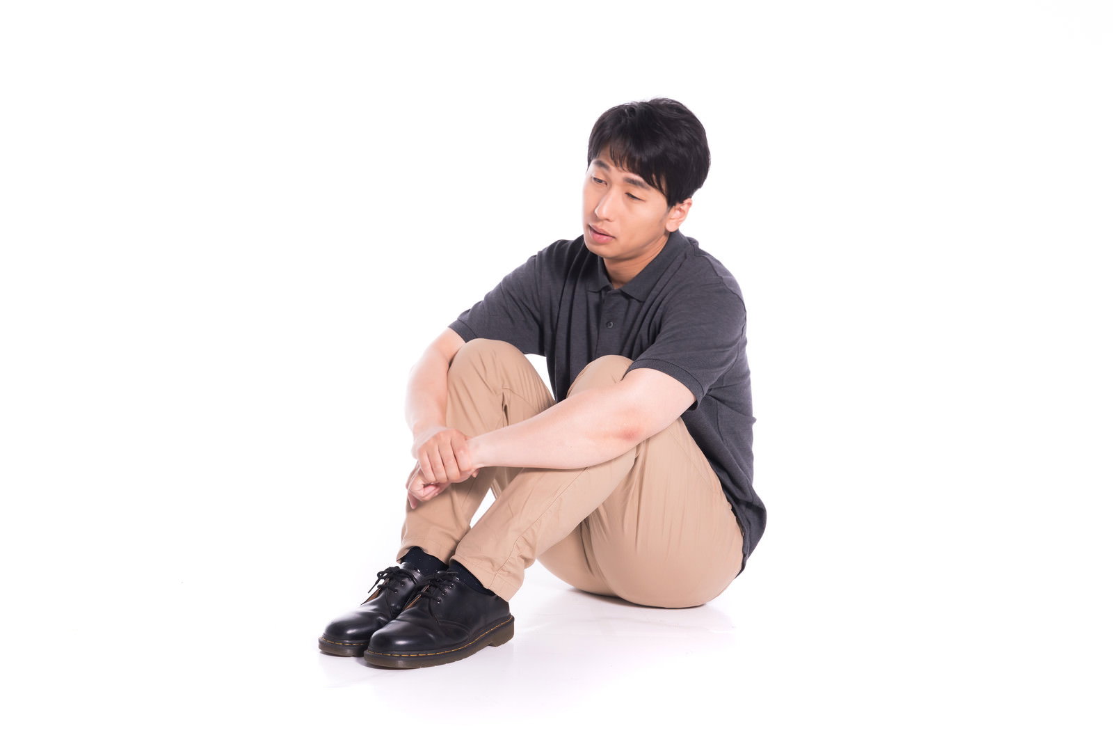 黒いTシャツを着た男性が体育座りで膝を抱えて座っている［モデル：大川竜弥］