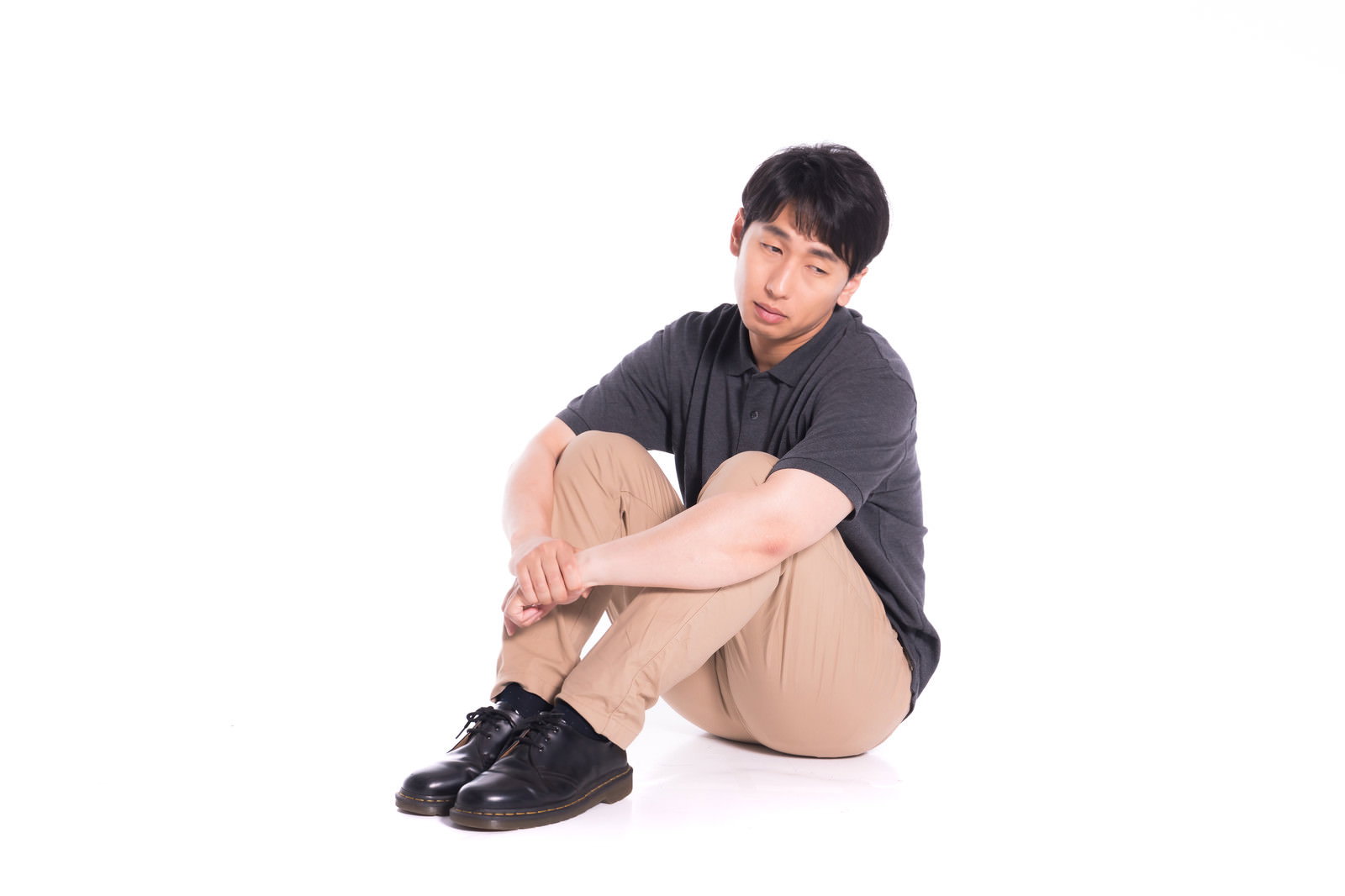 体育座りをして憂鬱そうにうつむく黒いTシャツの男性［モデル：大川竜弥］