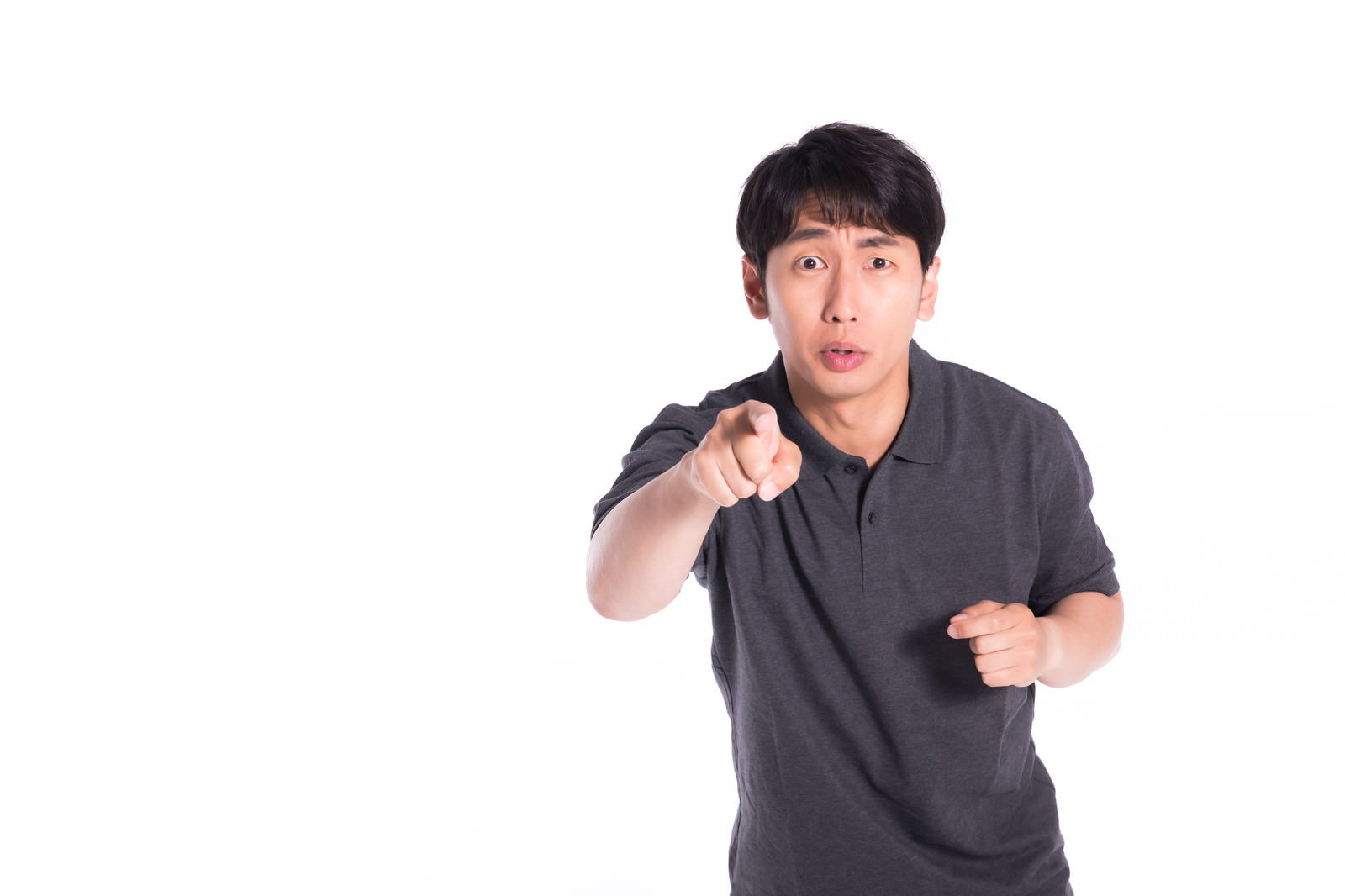 グレーのTシャツを着た男性が指を向けて怒りの表情を見せている［モデル：大川竜弥］