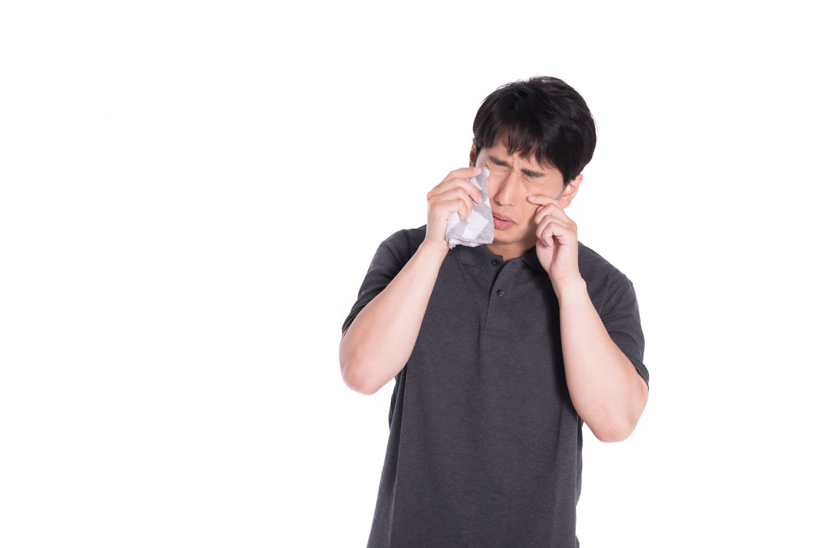 グレーのTシャツを着た男性がハンカチで涙を拭いている様子［モデル：大川竜弥］