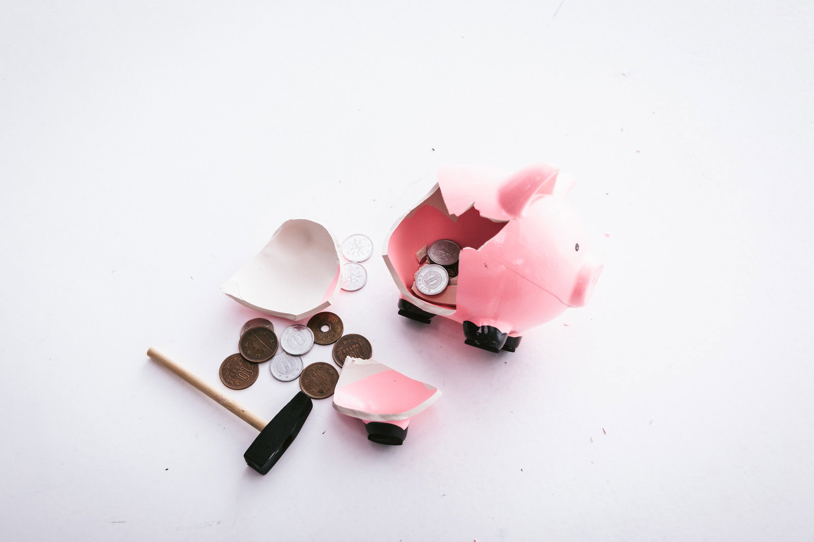 ハンマーで割られたピンクの豚の貯金箱から小銭が散らばっている