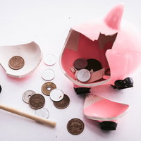 ハンマーで割られたピンクの貯金箱と散らばった硬貨の写真