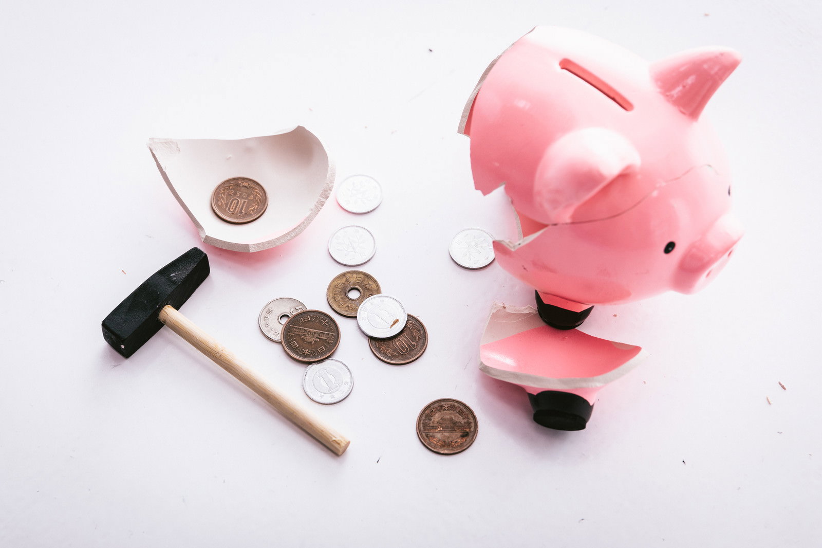 ハンマーで壊されたピンクの豚の貯金箱とわずかな小銭が散らばっている様子