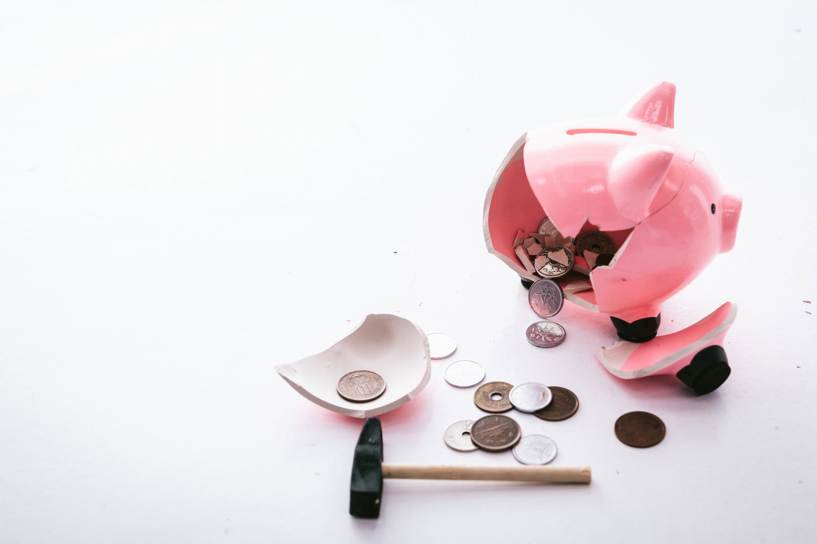 割れたピンクの豚の貯金箱から散らばった硬貨とハンマー