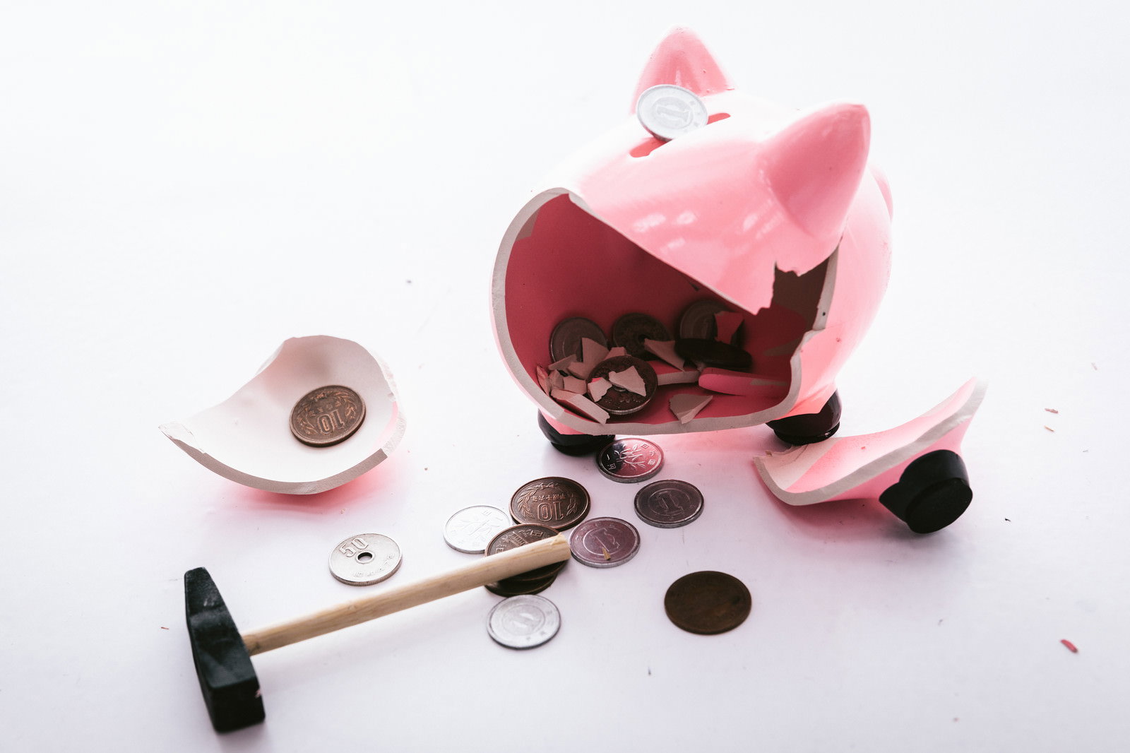ハンマーで破壊されたピンク色の豚の貯金箱と散乱した小銭
