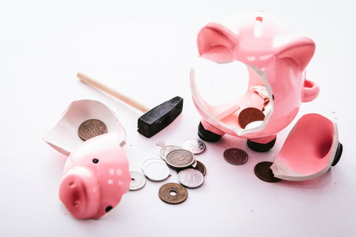 割れて硬貨が散らばったピンク色の豚の貯金箱