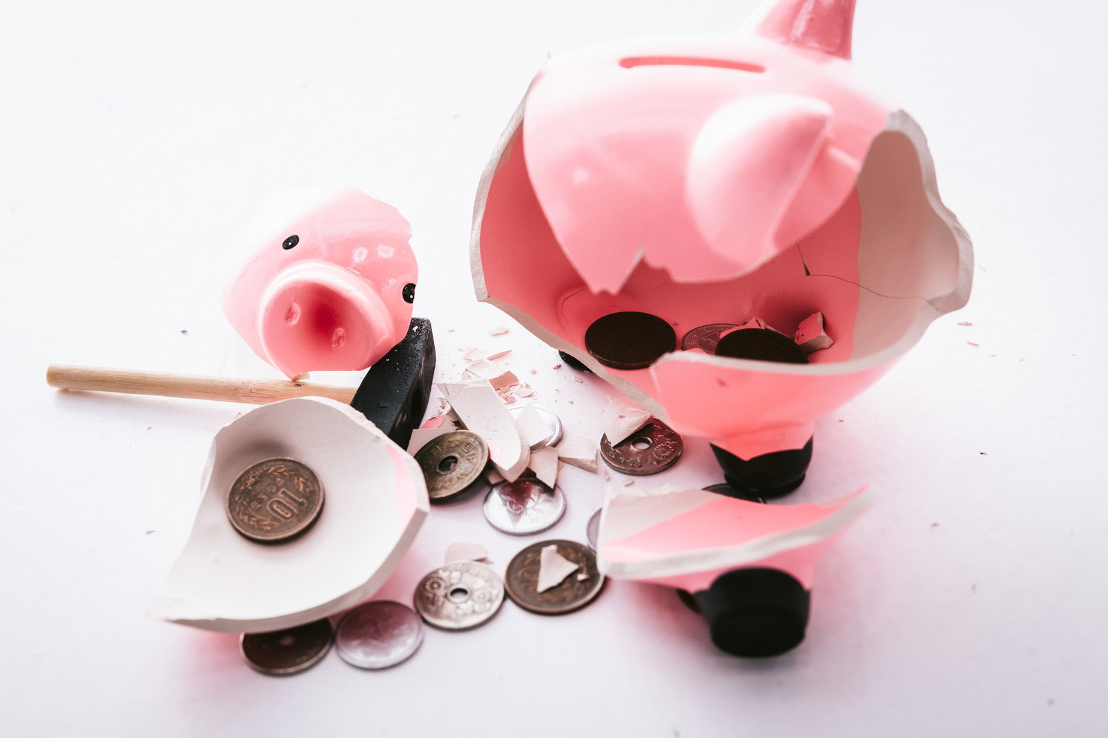 割れたピンク色の豚の貯金箱から散らばった小銭とハンマー