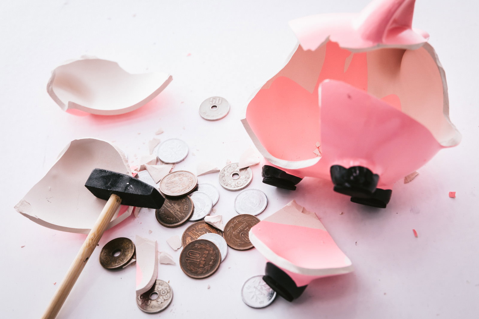 白い背景に割れたピンクの貯金箱と散らばった硬貨