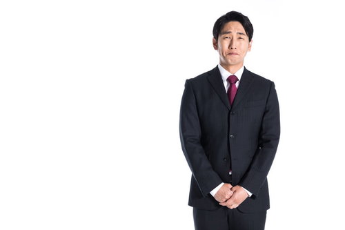口をつぐんでじっと我慢をする黒いスーツの会社員男性