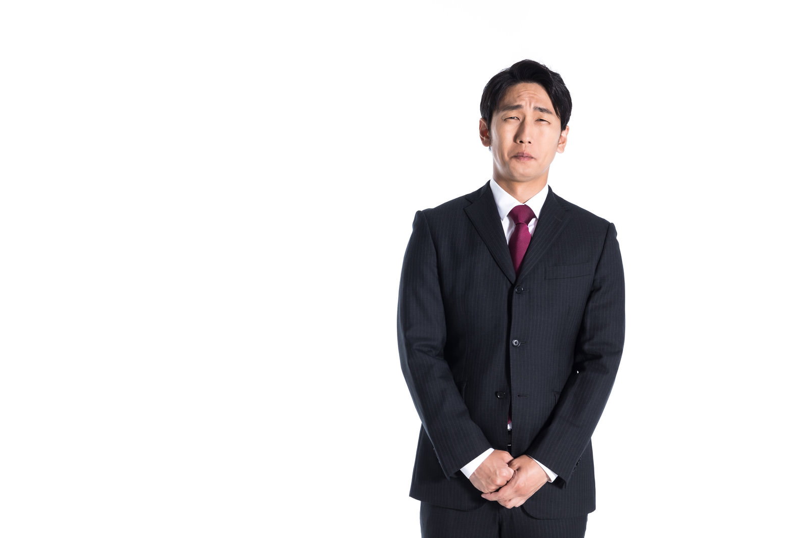 申し訳なさそうな表情で立っている黒いスーツの会社員男性［モデル：大川竜弥］