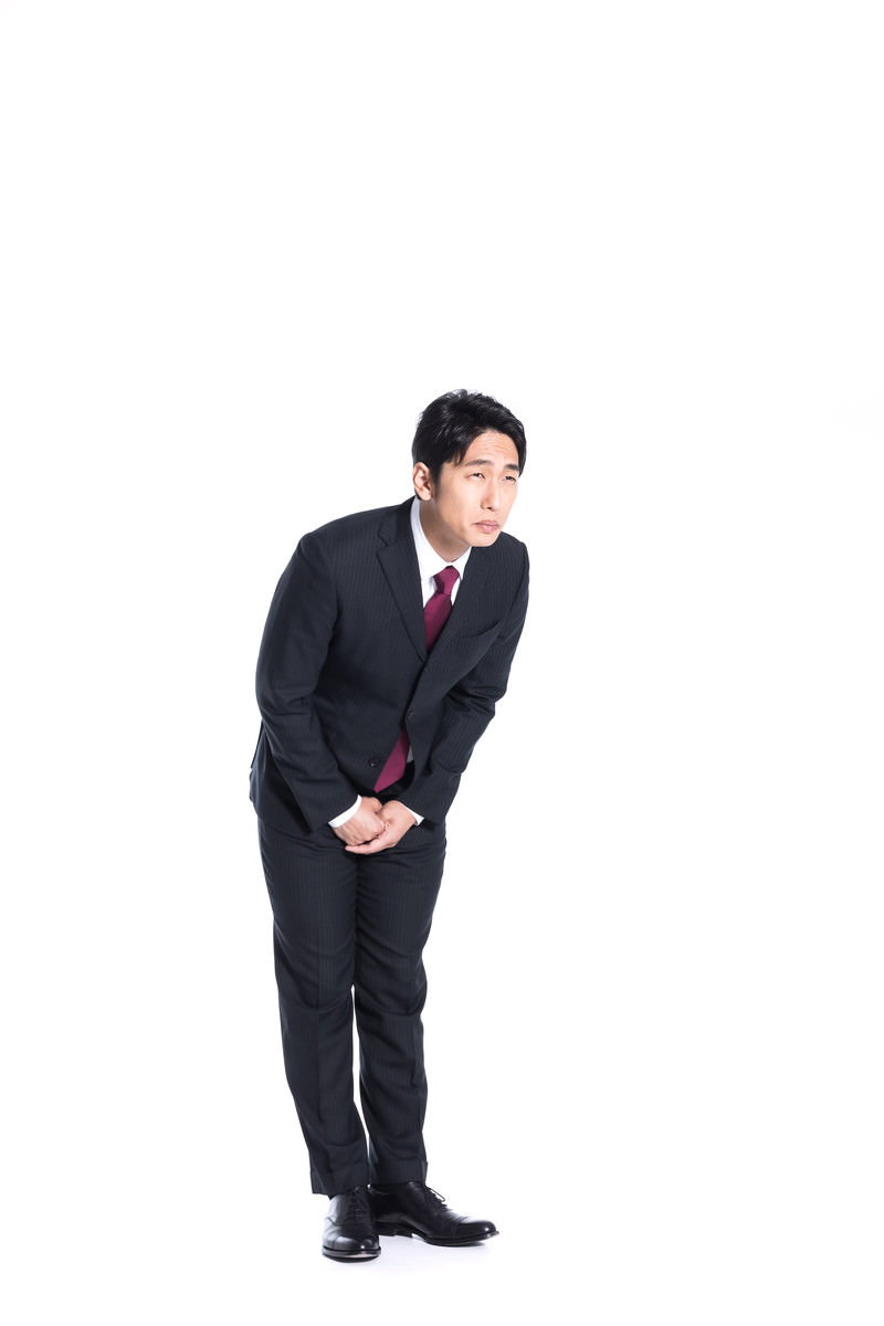 黒いスーツを着た男性が腰を深く折り曲げてお辞儀をしている［モデル：大川竜弥］