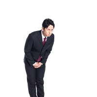 涙をこらえながら深くお辞儀をして謝罪するスーツ姿の男性の写真