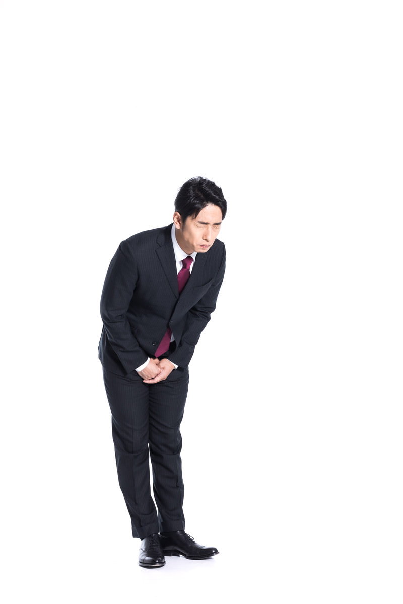 涙をこらえながら深くお辞儀をして謝罪するスーツ姿の男性［モデル：大川竜弥］