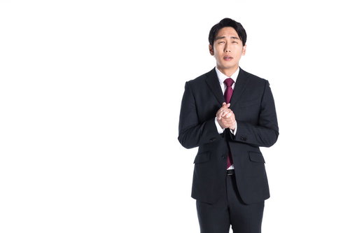 黒いスーツを着てもみ手をする営業マンの謝罪ポーズ