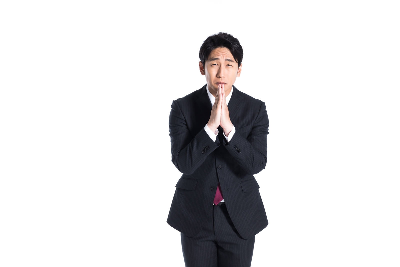 黒スーツの男性が両手を胸前で合わせ、不安げな表情で懇願するポーズをとっている［モデル：大川竜弥］