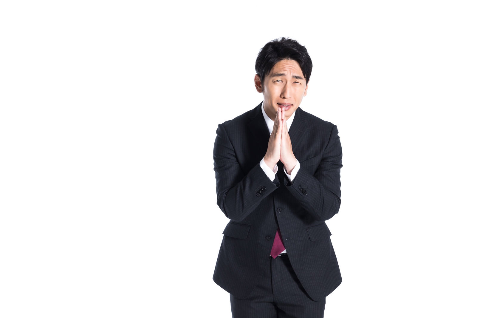 黒いスーツ姿の男性が両手を合わせて頭を下げるポーズをしている［モデル：大川竜弥］