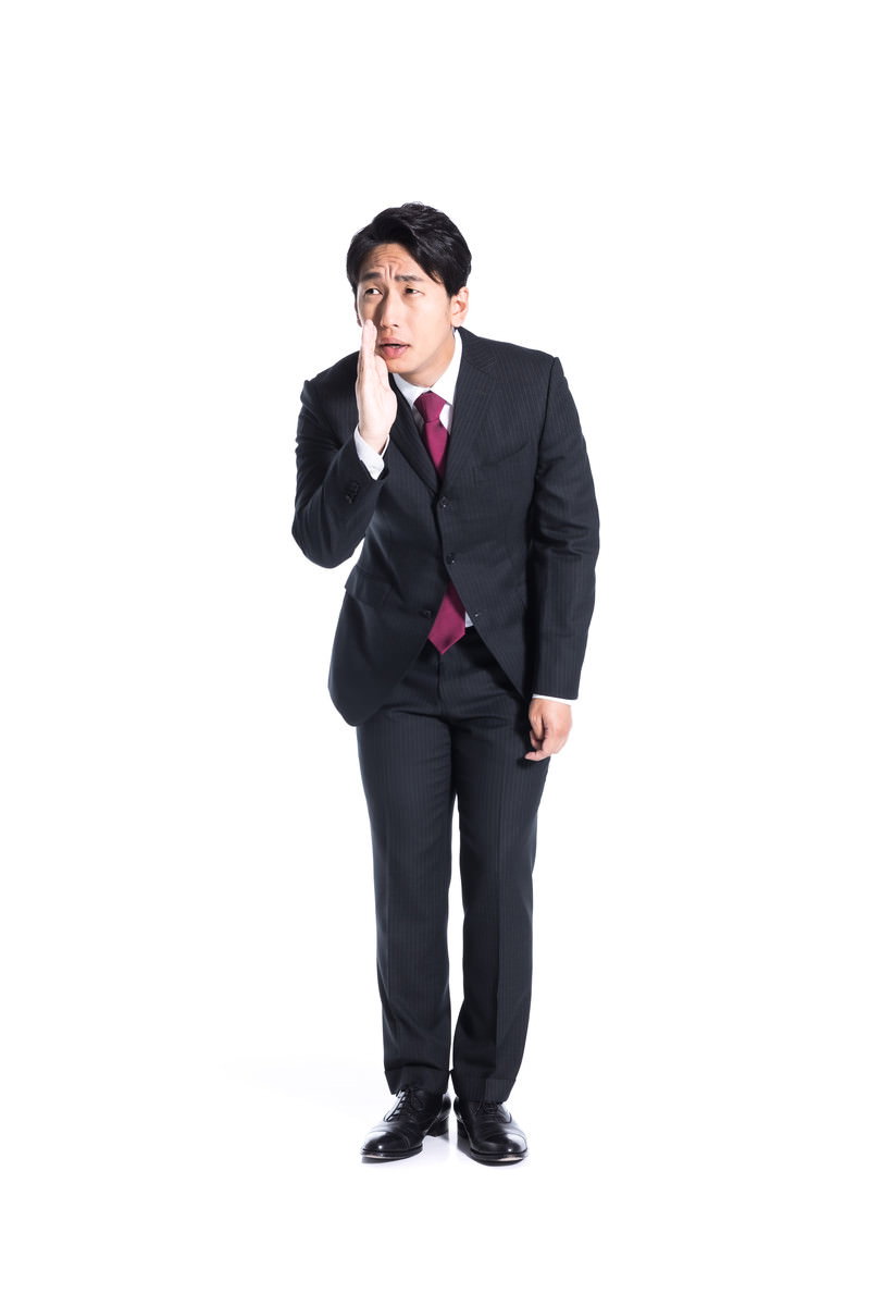 スーツを着た男性が手を口元に当てて内緒話をしている［モデル：大川竜弥］