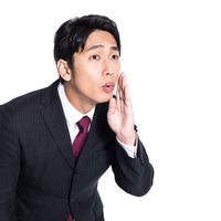 小声でデマを流すスーツの男性の写真