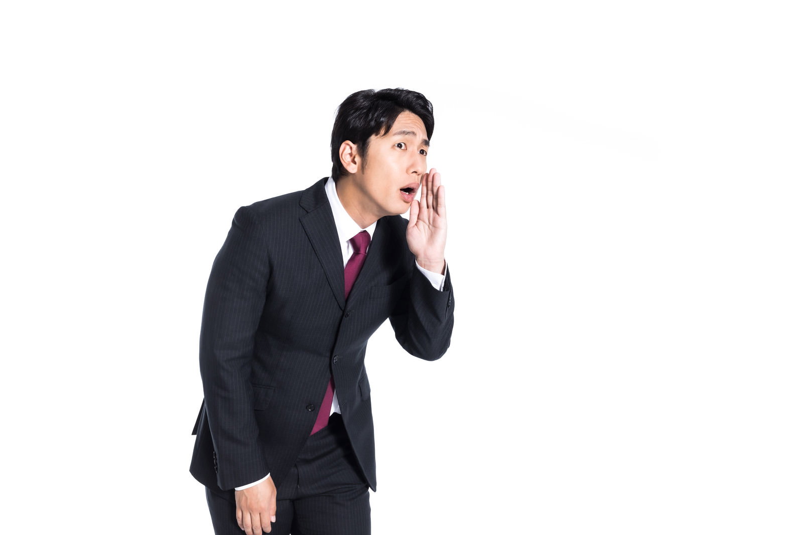 スーツ姿の男性が手を口に当てて小声で話している［モデル：大川竜弥］