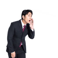 スーツの男性が手を口に当てて他社の悪評を流すクレーマーの写真