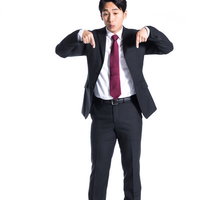 両手で足元のポイントを指差す紺色スーツの男性の写真
