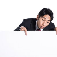 画面下のテロップを指さす黒いスーツの男性タレントの写真