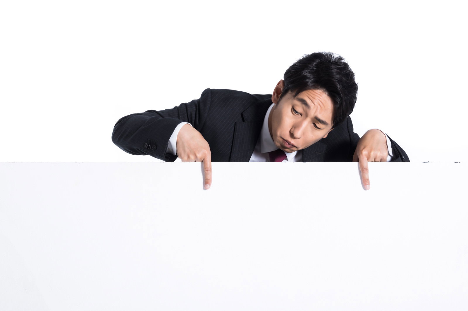 白いボードから困った表情で覗き込み指をさす黒いスーツの男性［モデル：大川竜弥］