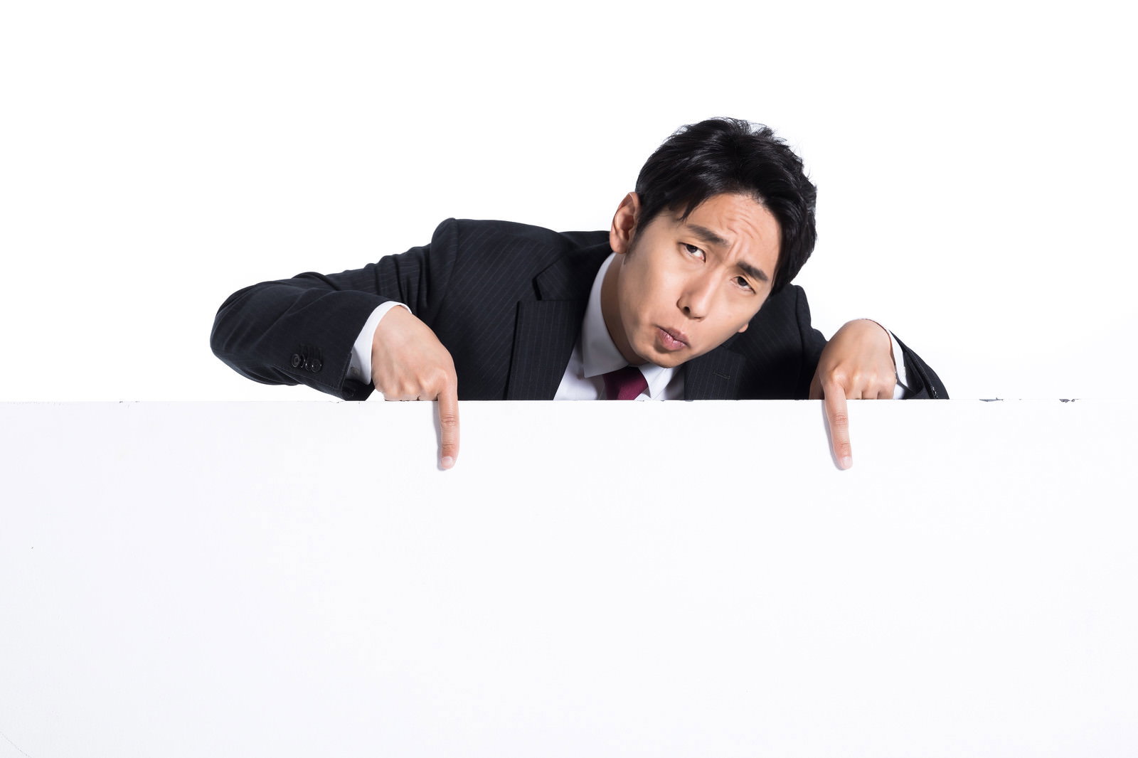 白いホワイトボードの上から顔を出し、両手の指でボード下部を指して注意を促すビジネススーツの男性
