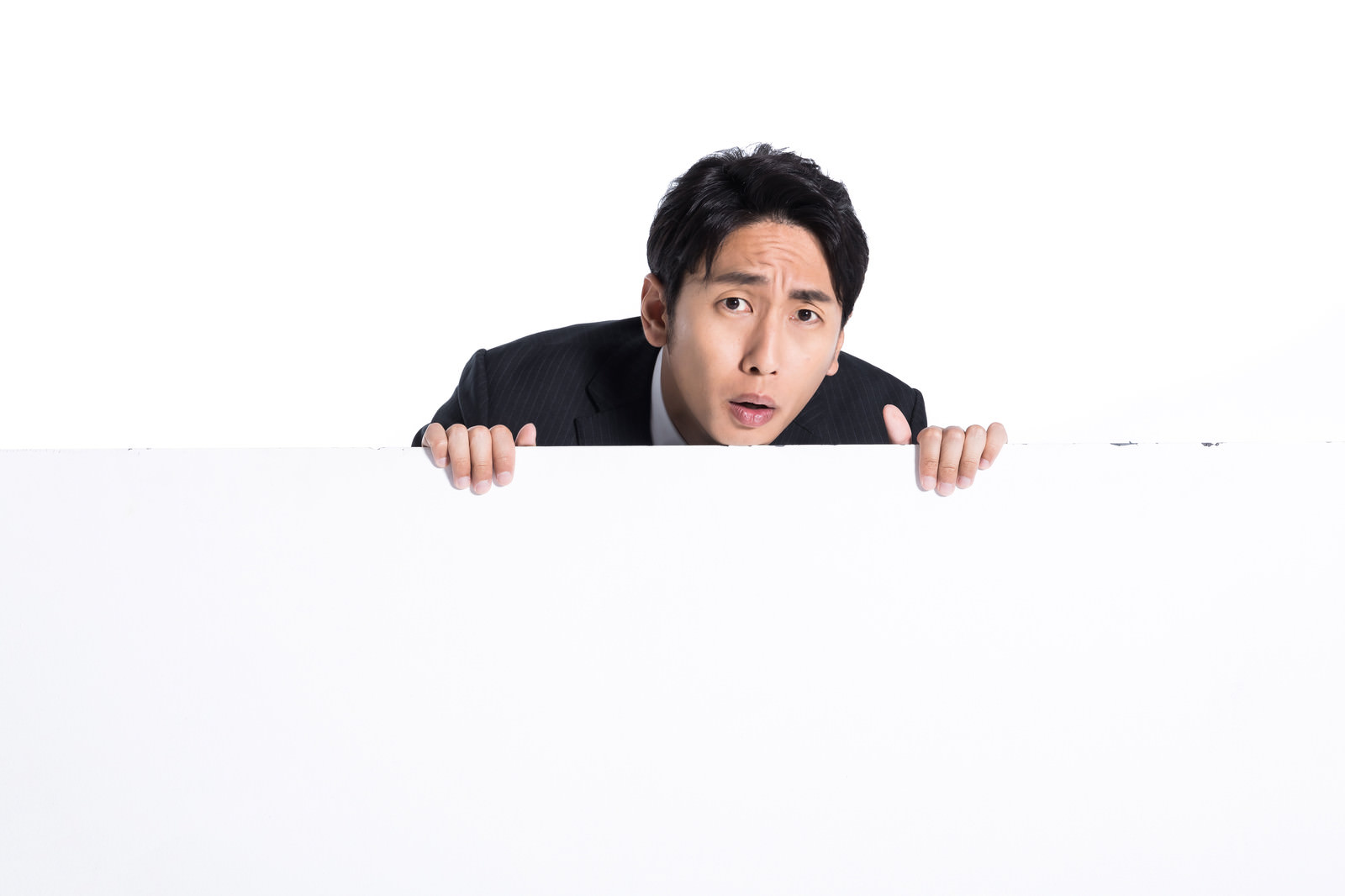 白い看板の後ろから驚いた表情で顔を出している男性［モデル：大川竜弥］