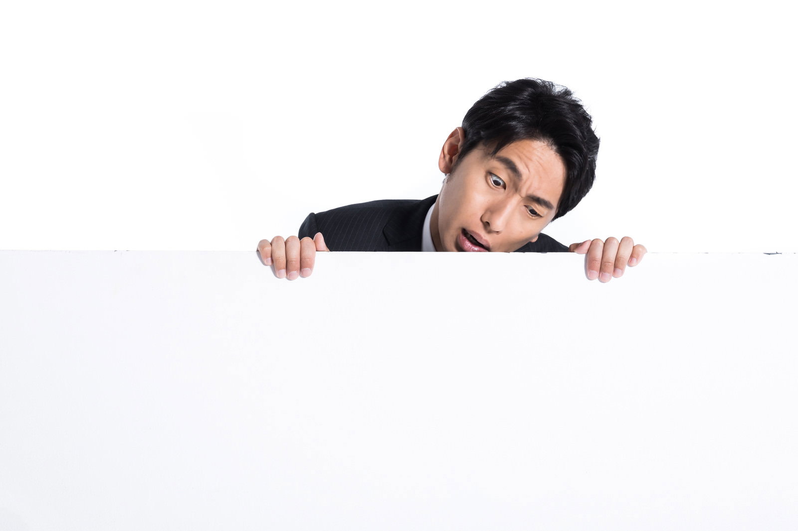 白い板パネルから顔を出し、眉をひそめて怒った表情をする黒髪の男性［モデル：大川竜弥］