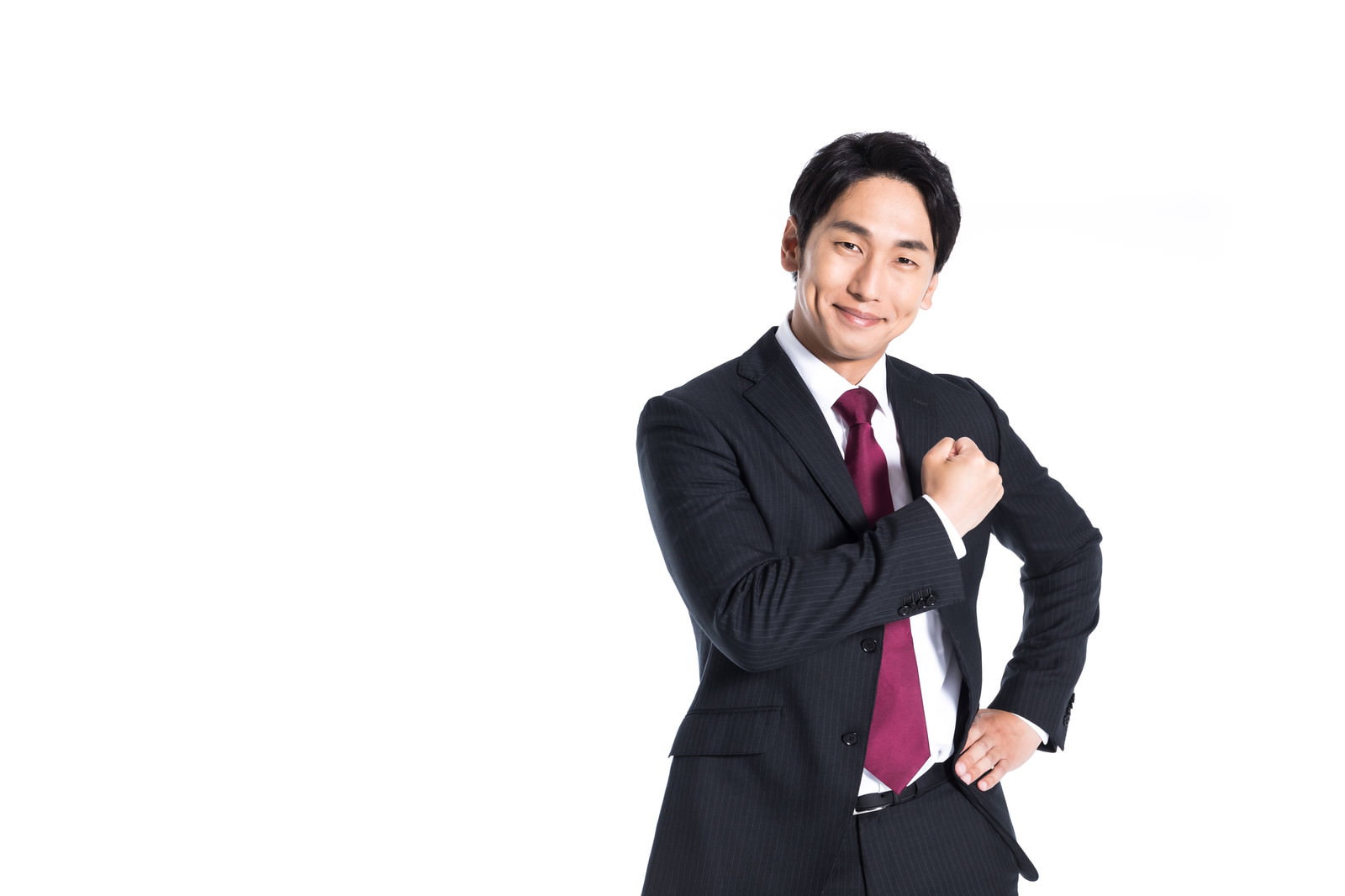 黒いスーツに赤いネクタイを着用した男性がガッツポーズをしている［モデル：大川竜弥］