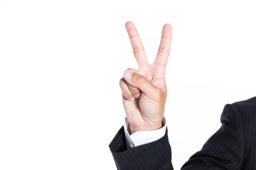 スーツ姿でピースサインを作る男性の指二本