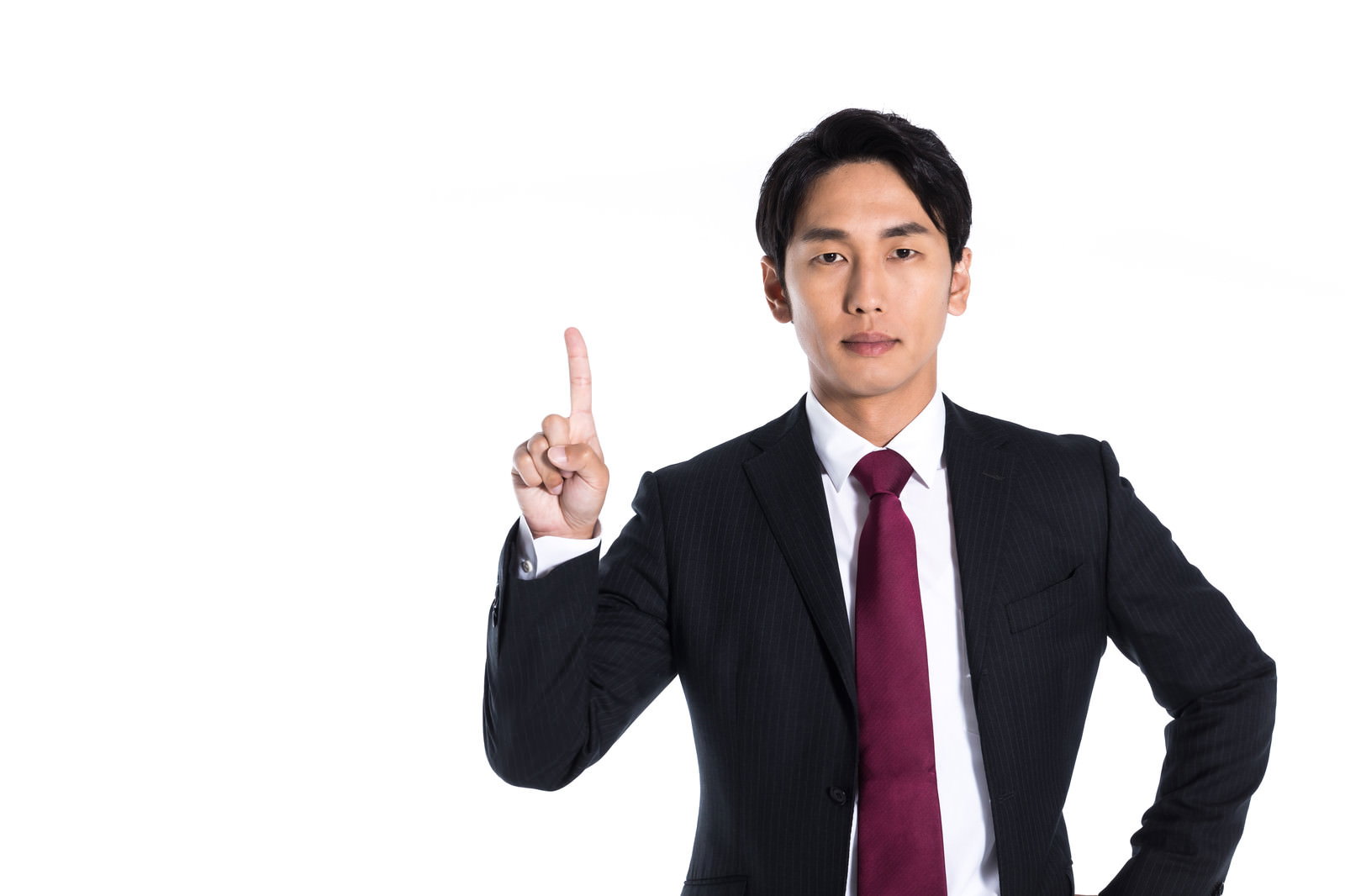 紺のスーツに赤ネクタイ姿の男性が、右手の人差し指を上に立てて指し示す［モデル：大川竜弥］